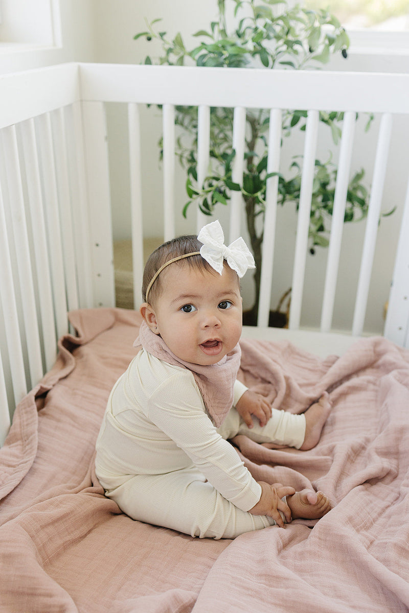 Draped in a nursery setting, the Mebie Baby Dusty Rose Muslin Quilt serves as a gentle muslin throw blanket.