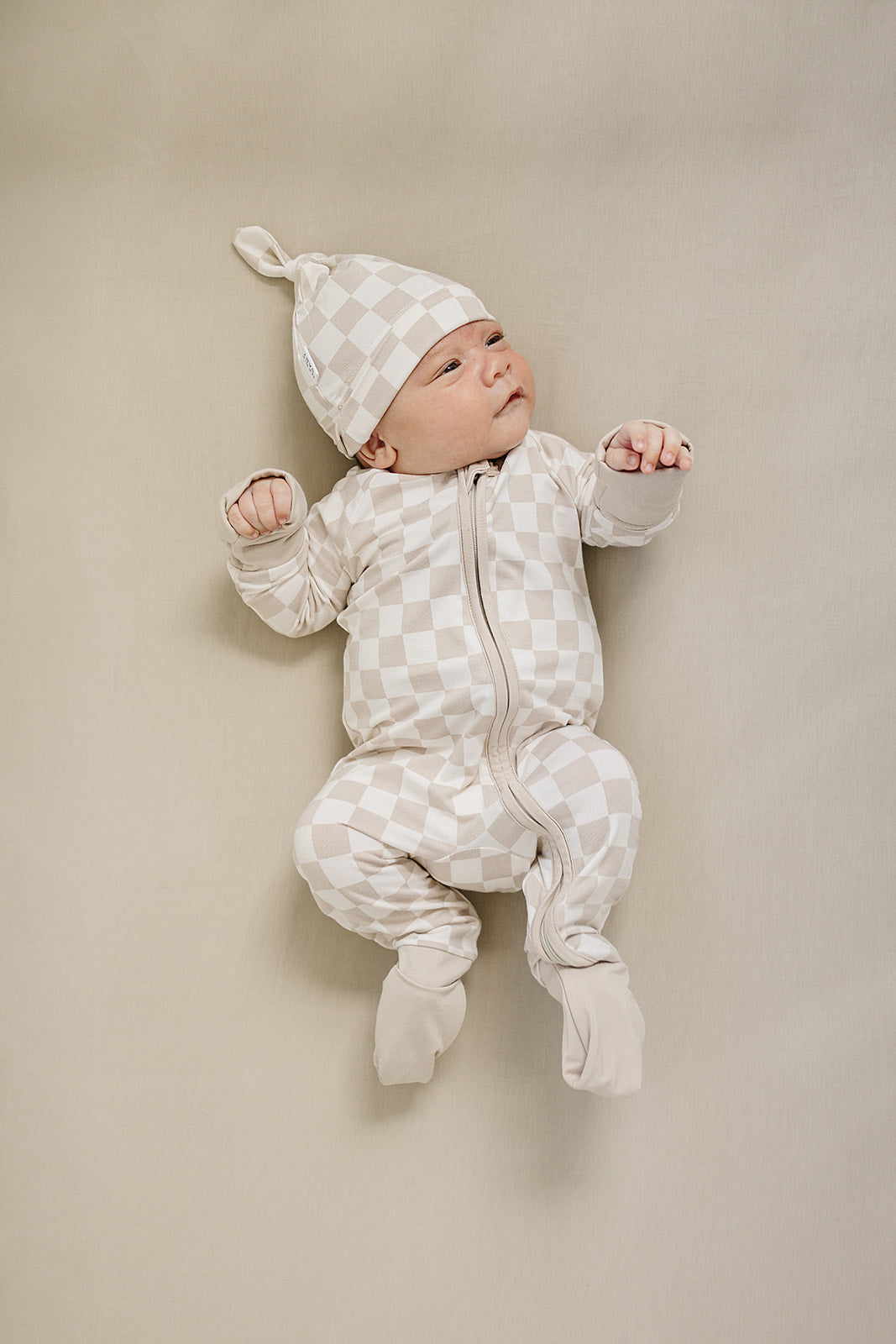 Styled flat lay of the Taupe Checkered Bamboo Zipper, a popular nursery favorite from Mebie Baby