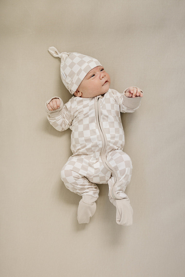 Styled flat lay of the Taupe Checkered Bamboo Zipper, a popular nursery favorite from Mebie Baby