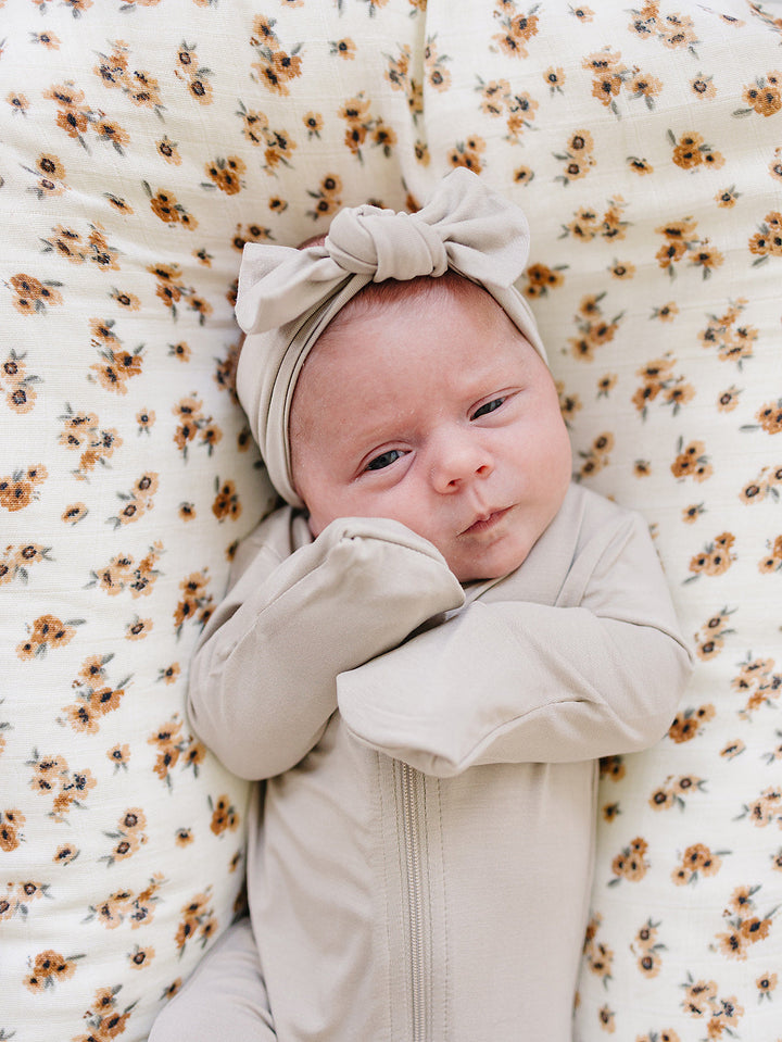 Oatmeal Bamboo Footed Zipper folded next to a stuffed toy, an organic cotton footie pajama for babies.