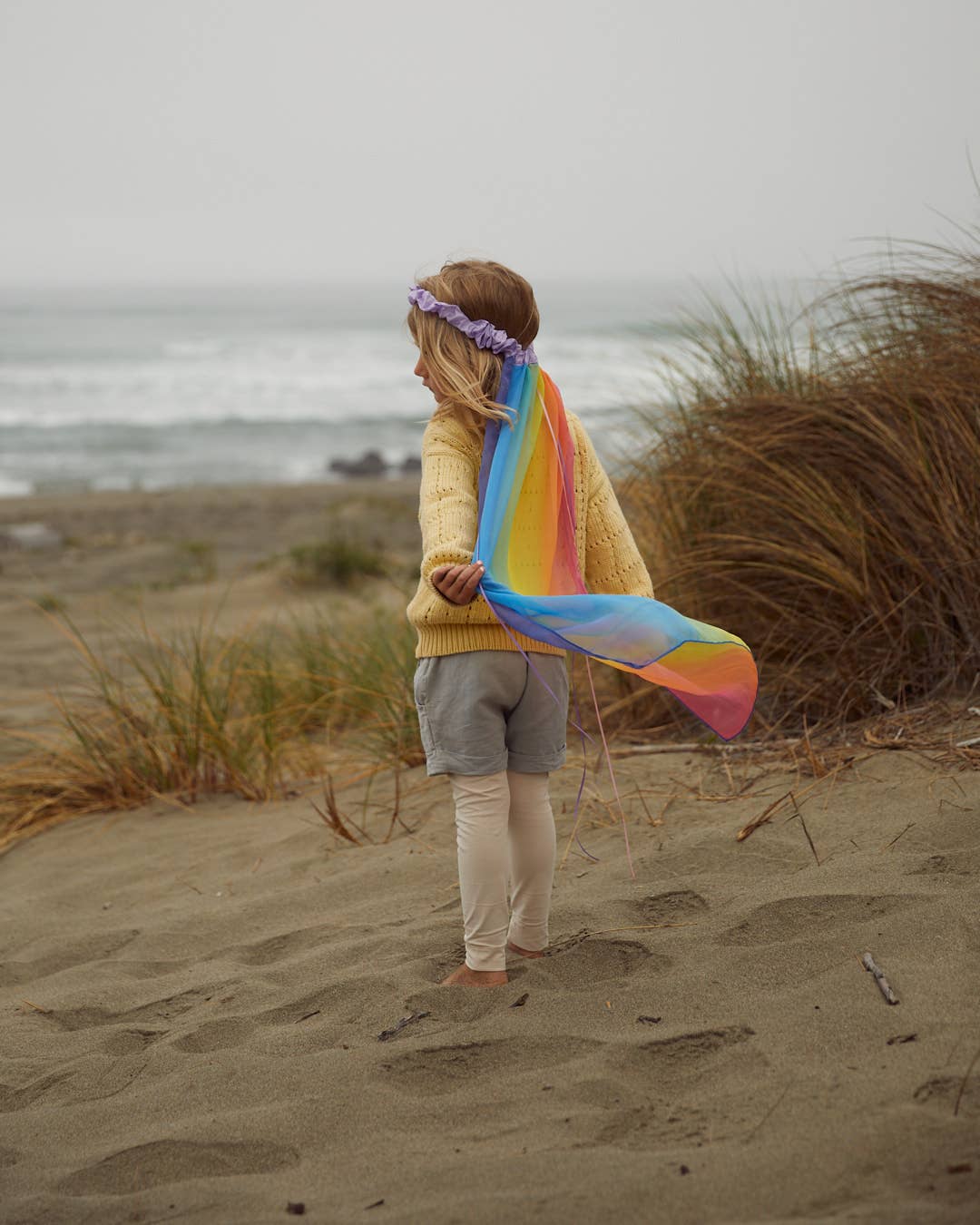 Beloved by little ones, child wearing the Sarah's Silks Rainbow Veil on a beach walk