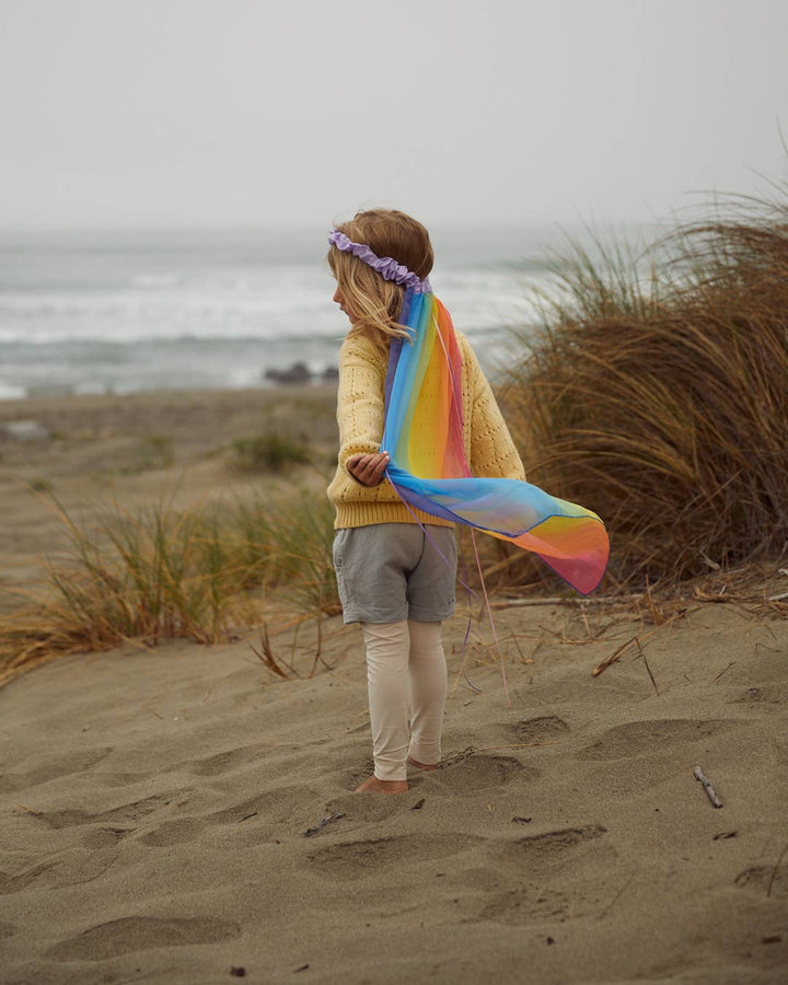 Beloved by little ones, child wearing the Sarah's Silks Rainbow Veil on a beach walk
