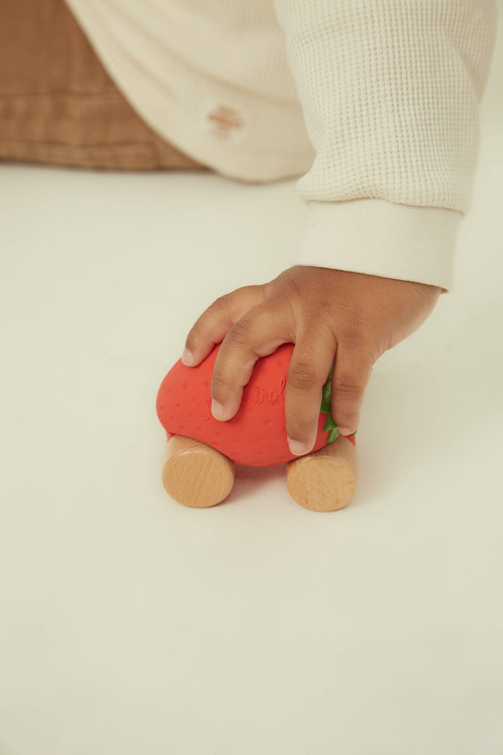 A hand holds the Oli & Carol Sweetie the Strawberry Baby Car to show its compact size