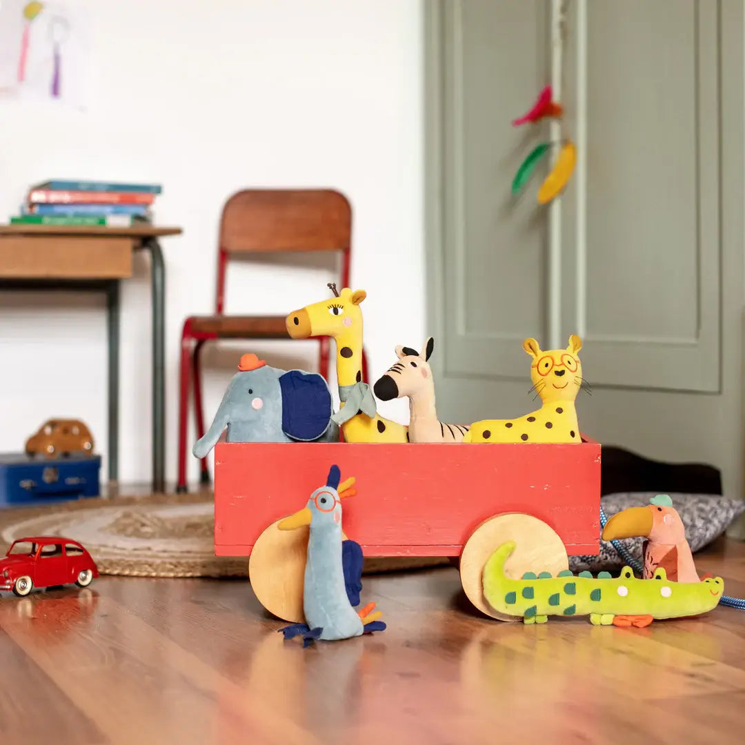 Moulin Roty Colorful toy animal rattles in a red wagon on a wood floor