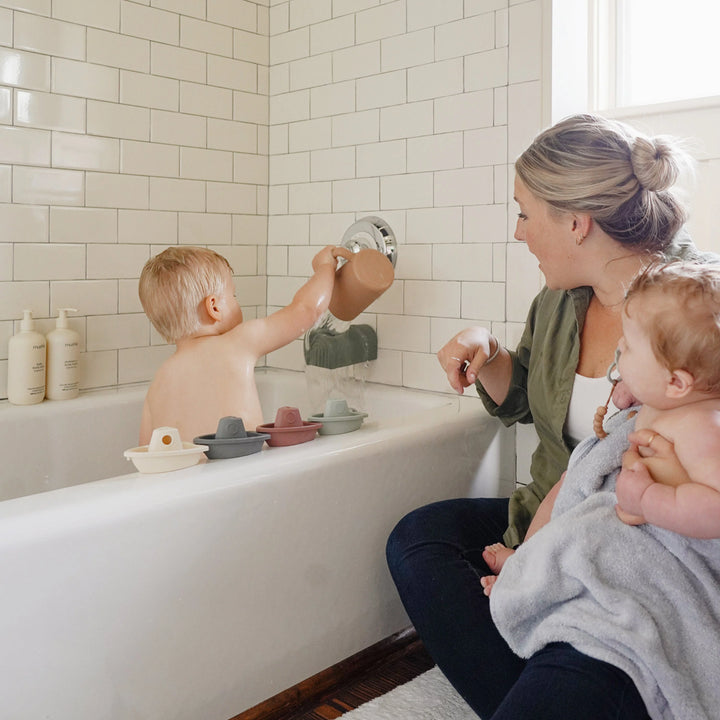 infant with mushie bath toy boats