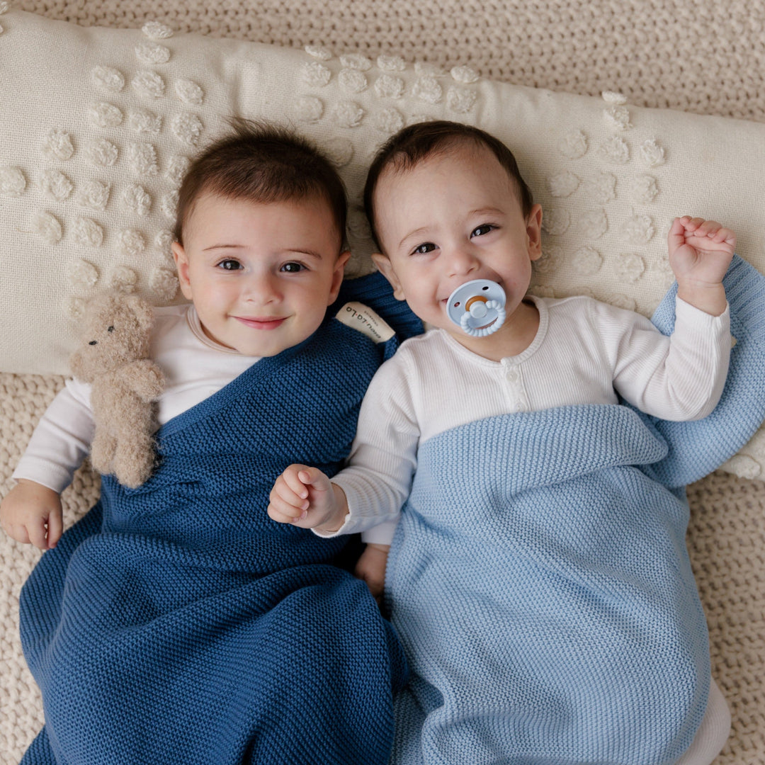 Two toddlers wrapped Bleu La La's Heritage Knit Cotton Swaddle, one in cobalt, the other in sky blue