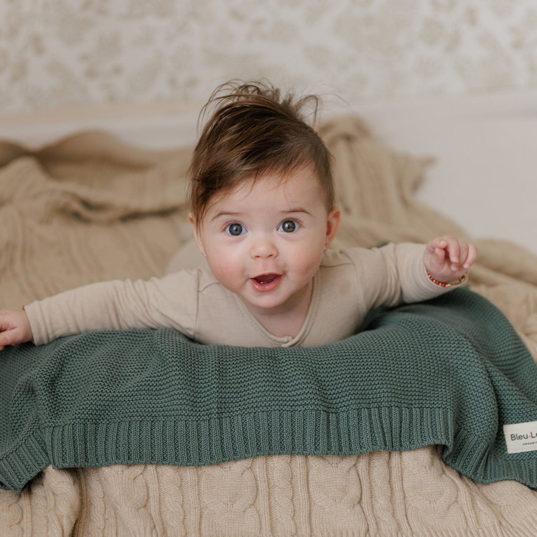 Baby lying on a bed on the Knit Heritage Blanket in Hunter Green, machine washable and durable