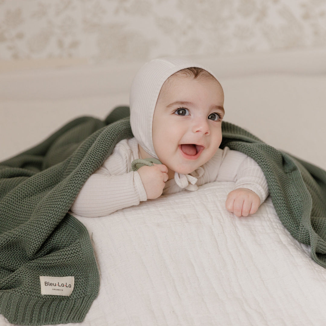 Baby under a Bleu La La Hunter Green Knit Heritage Cotton blanket, warm, breathable, and machine washable