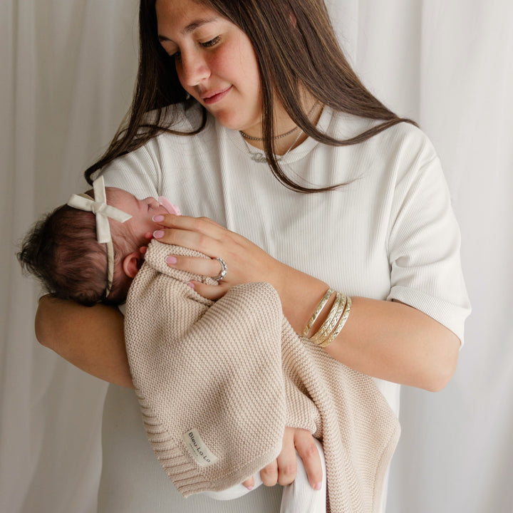 Woman holding a baby wrapped in a Bleu La La Heritage Knit Blanket in Oatmeal, the soft, breathable cotton 