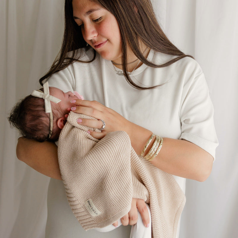 Woman holding a baby wrapped in a Bleu La La Heritage Knit Blanket in Oatmeal, the soft, breathable cotton 