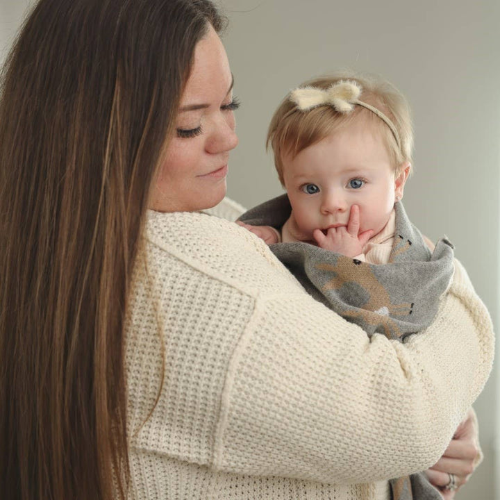 mother holding infant wrapped in knit cotton deer blu la la swaddling blanket 