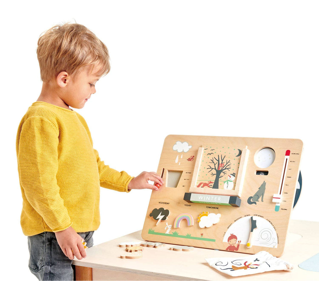 A boy in a yellow sweater reaches to explore the Tender Leaf Toys Weather Watch at the table