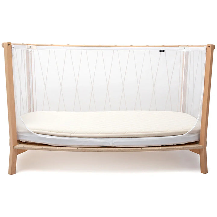 Softly lit interior shows the KIMI Evolving Baby Bed by Charlie Crane in hazelnut with a coconut fiber mattress