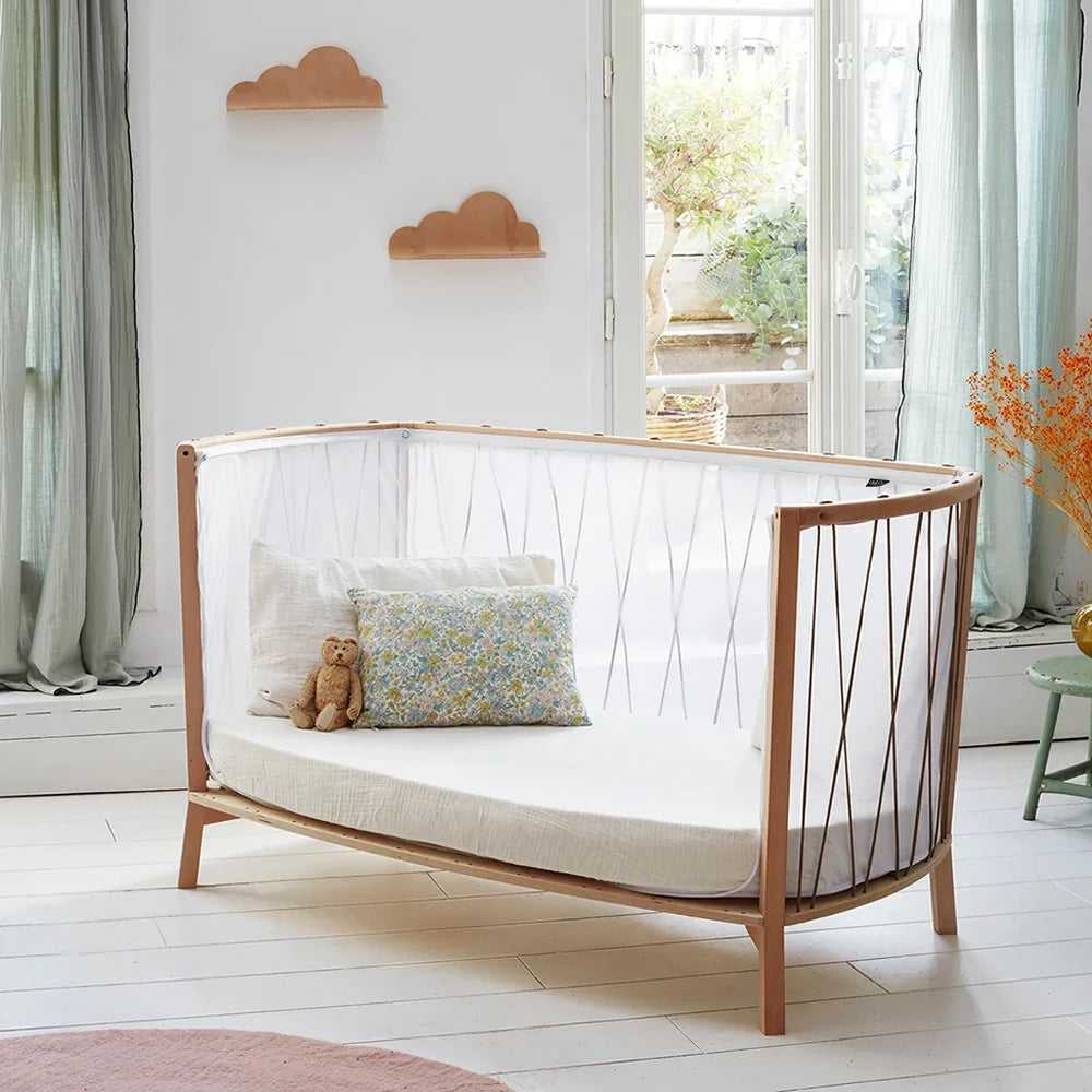 Angled nursery view shows the Charlie Crane KIMI Evolving Baby Bed in bois de rose with a midcentury modern design
