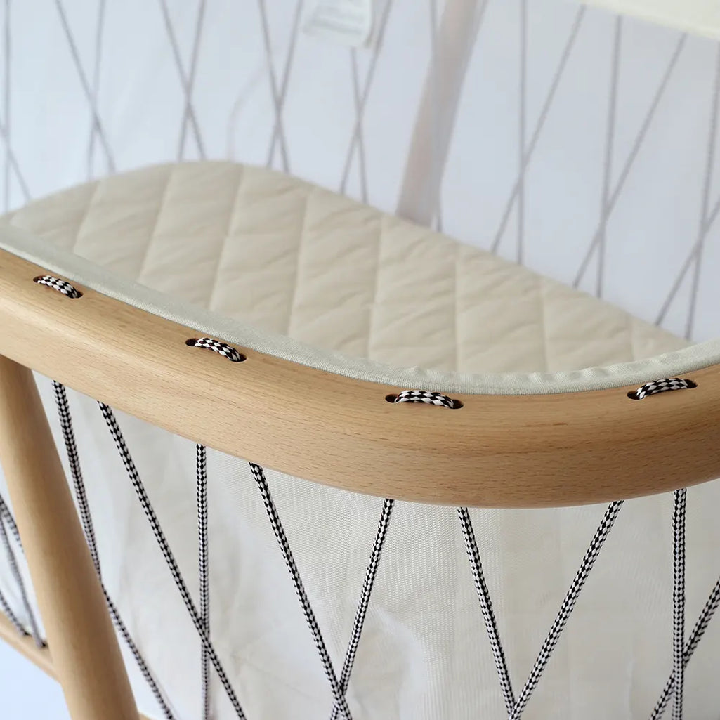 Balanced modern nursery scene shows the KUMI Charlie Crane Cradle in lichen with wooden elegance