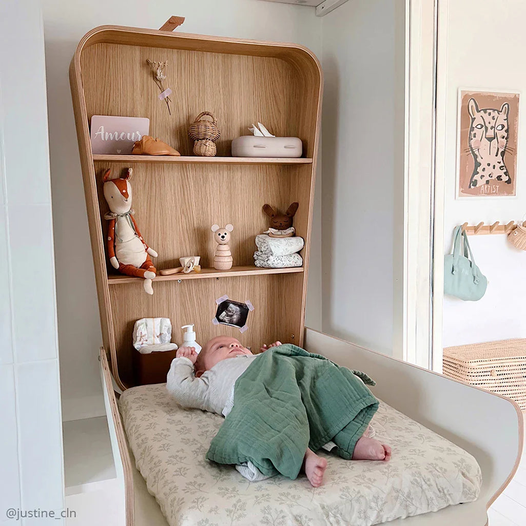 infant laging on pearl blossom charlie crane changing mat with lichen swaddle across knees 