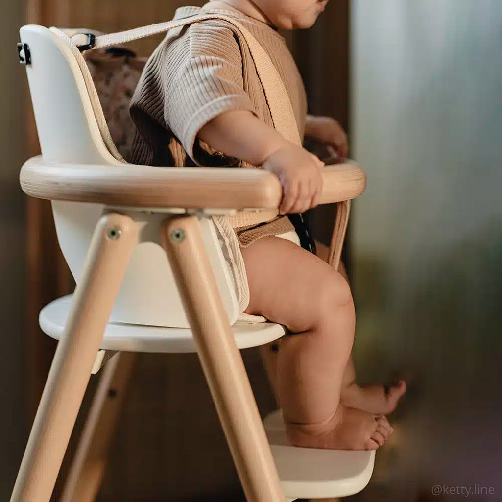 baby leaning forward in charlie crane high chair baby set showcasing infant safe straps 