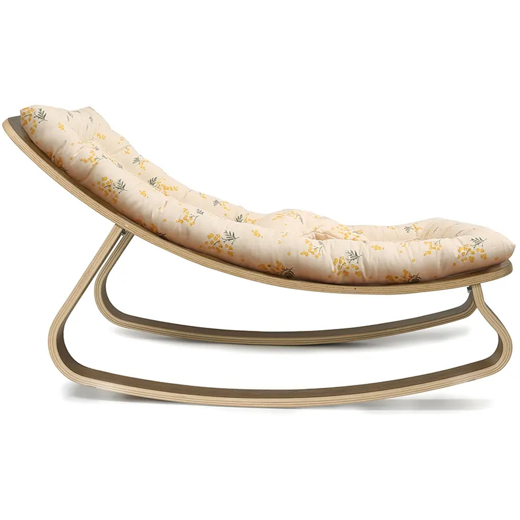Side profile of the Charlie Crane Walnut Wood Levo Rocker in organic milk, designed with a rounded shape for infant comfort