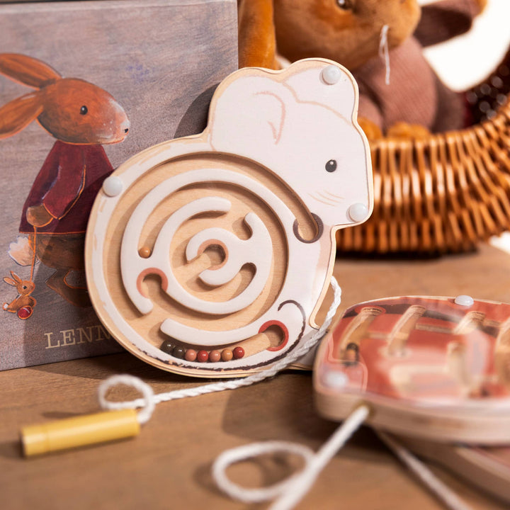 A mouse maze from Egmont's Mini Magnetic Color Maze rests on a wooden table near a rabbit figurine