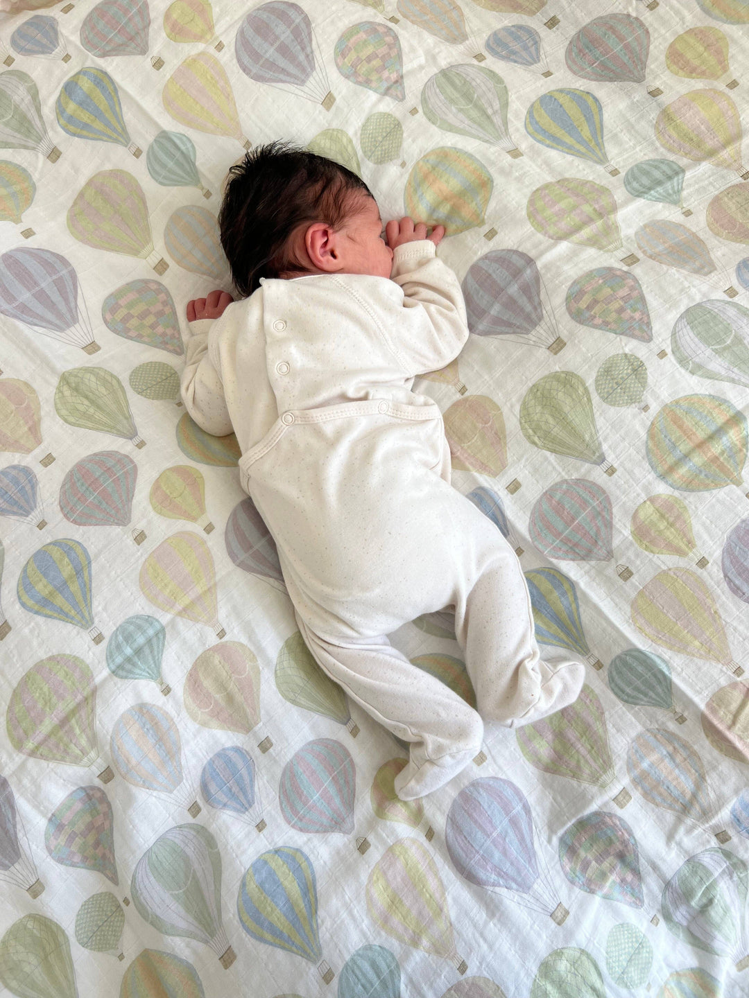 Newborn resting on Little Threads pastel air balloon muslin blanket, soft swaddle blanket for comfort, warmth, and supervised lounging