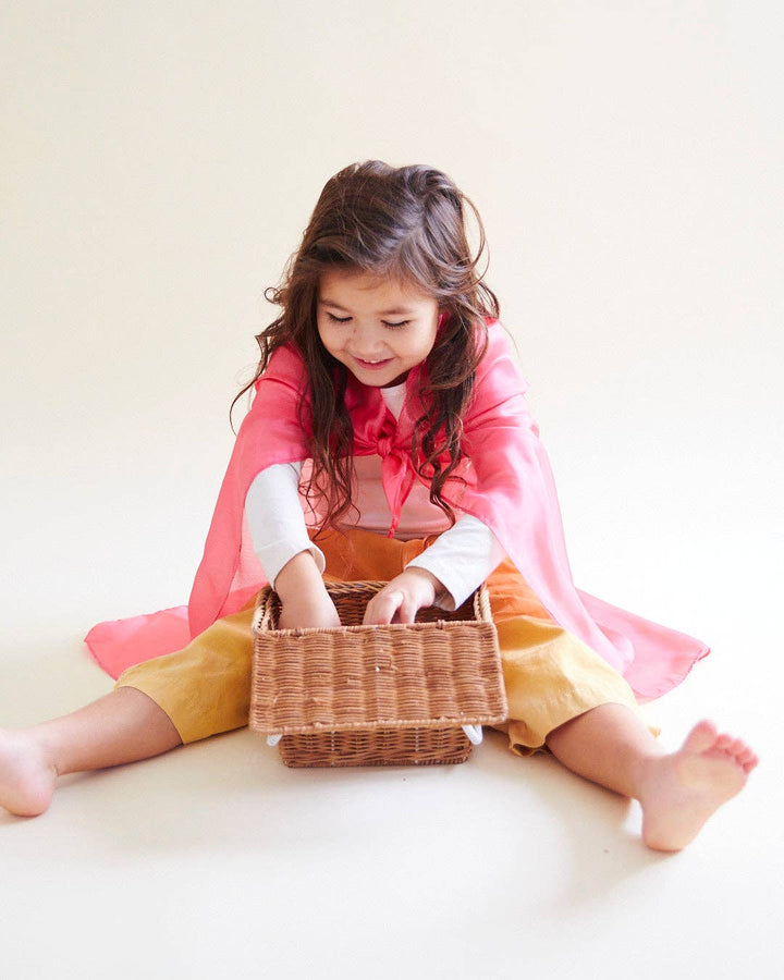 Sarah's Silks Solid Color Playsilk, an open ended play favorite, child sitting in a basket wrapped in pink silk