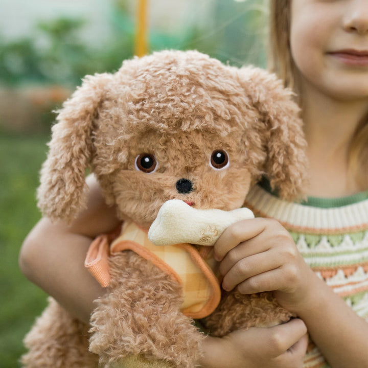 Child cuddling Dinkum Dogs Goldie golden plush puppy holding a bone treat outdoors