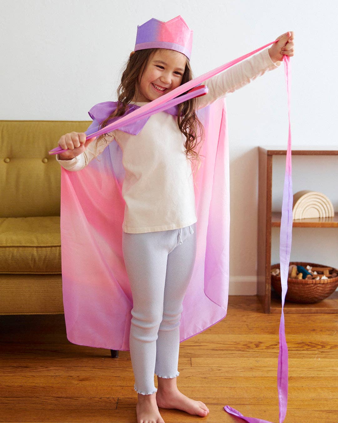 Reaching a silk ribbon overhead, a child plays pretend in the Sarah's Silks Blossom Cape