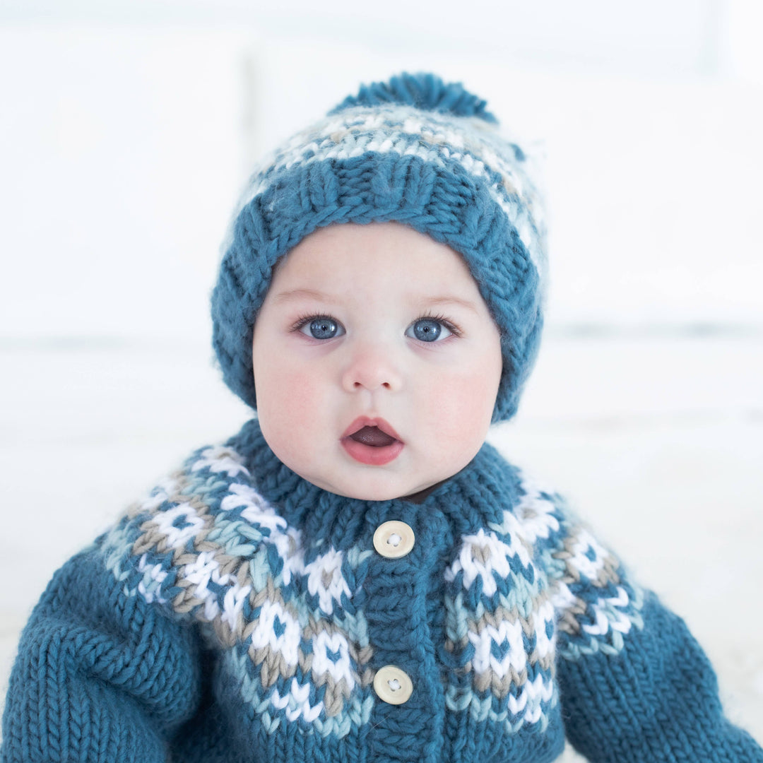 Close-up of baby in Huggalugs Fairisle Slate beanie and cardigan, pom-pom hat detail