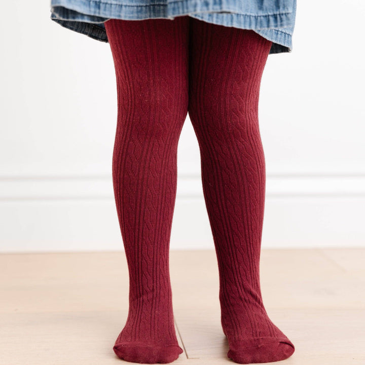 Toddler standing in Little Stocking Co. Burgundy Cable Knit Tights paired with a chambray dress