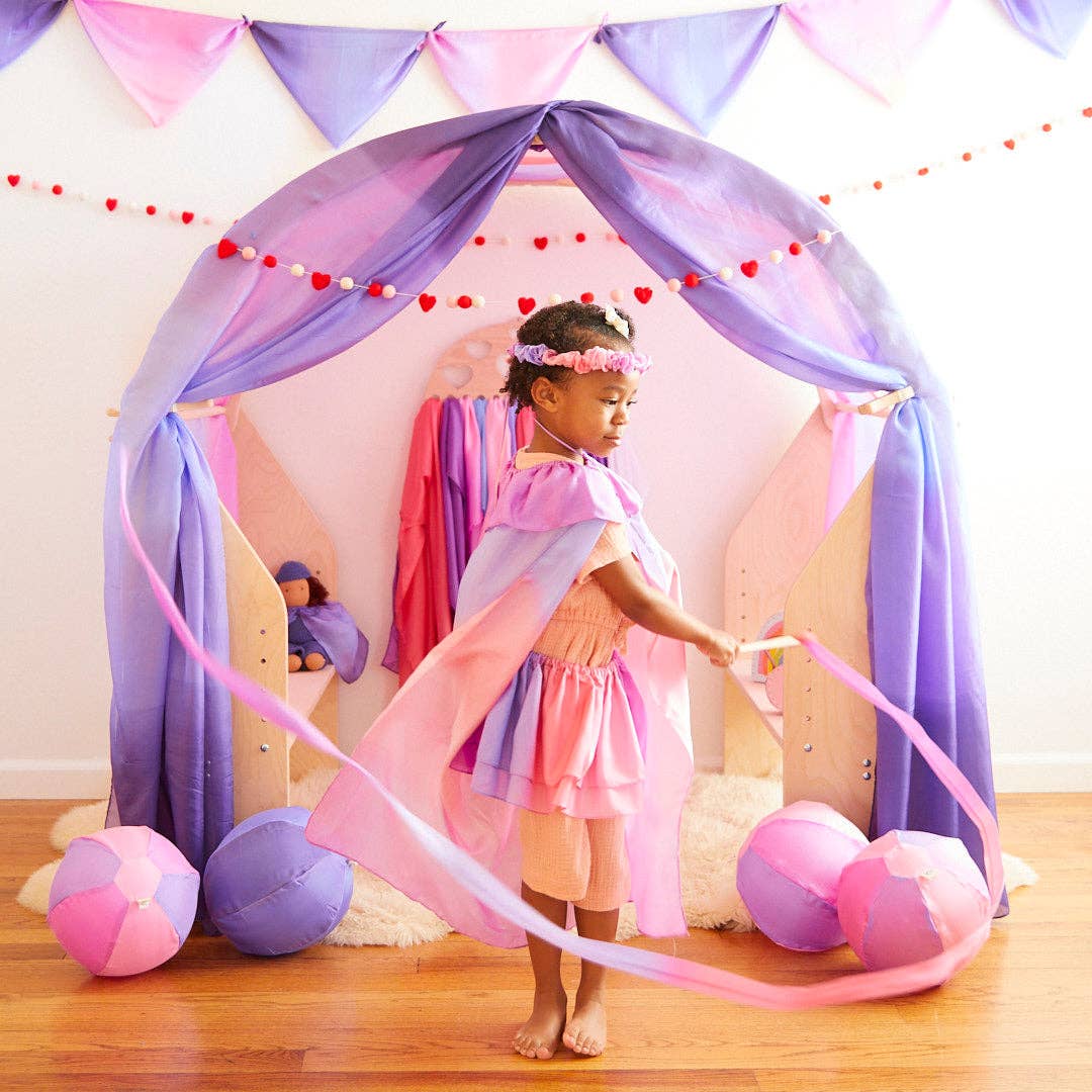 The Sarah's Silks Blossom Cape flows wide as a child spins among pastel balloons