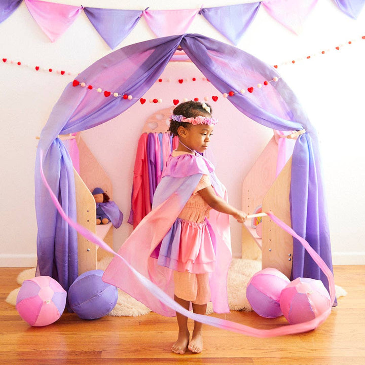 The Sarah's Silks Blossom Cape flows wide as a child spins among pastel balloons