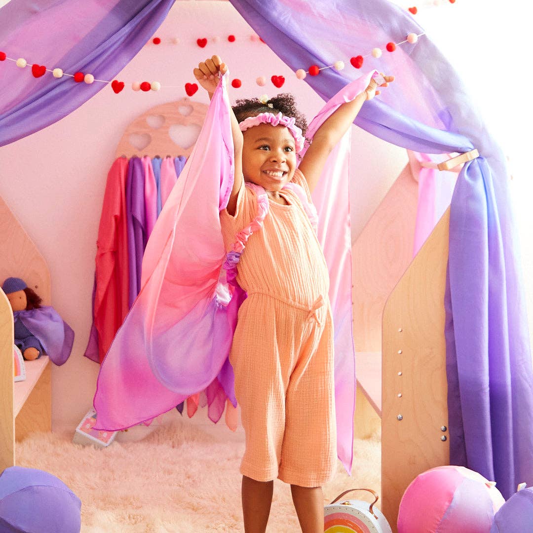 Reaching up in a silk cape, a child models the Sarah's Silks Blossom Garland among balloons