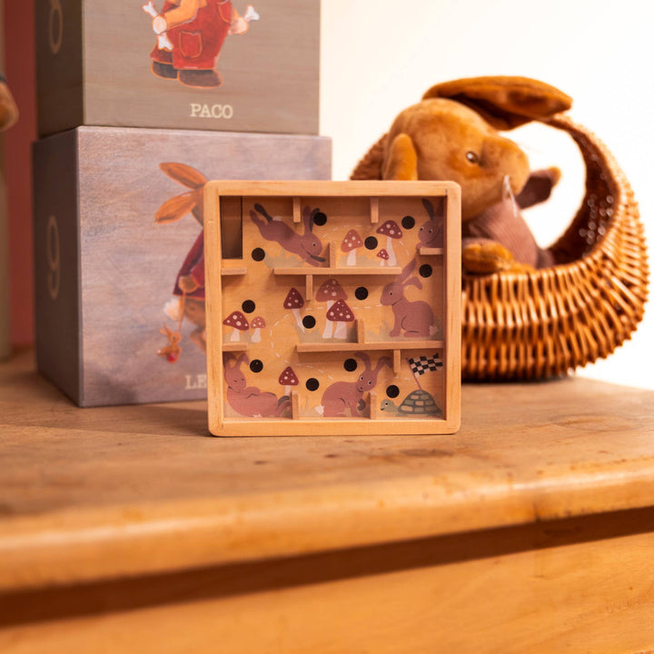 A Mini Wooden Labyrinth by Egmont sits on a wooden shelf beside a woven basket and gift boxes