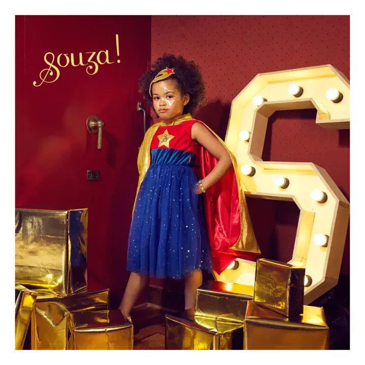 Girl in the Souza superhero costume standing in front of a large number '6' with gold presents
