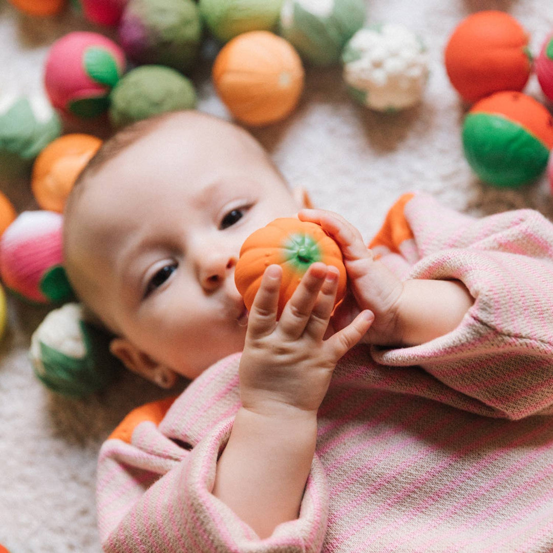 Baby reaches for a pumpkin ball while playing with Oli & Carol Veggie Soup Baby Sensory Balls