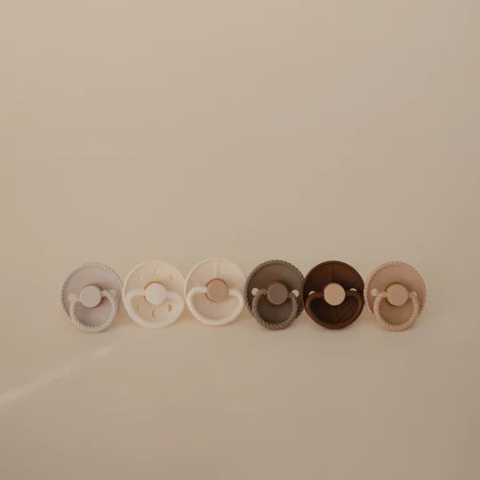 FRIGG Earthy Wonder pacifier 6-pack flat lay - warm-toned orthodontic baby pacifiers on minimal background