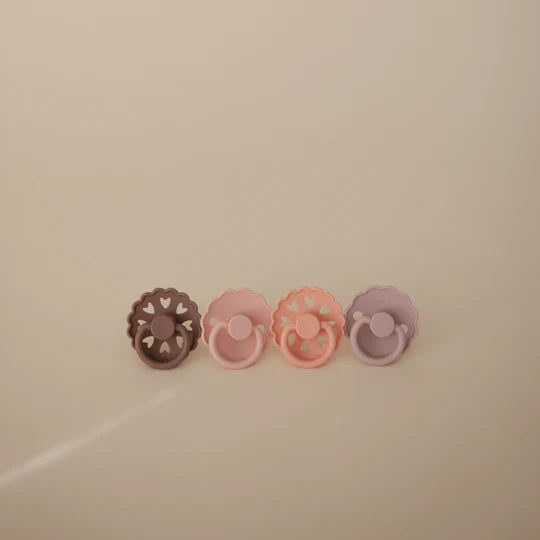 FRIGG Sunset Bliss rubber pacifier flat lay - warm sunset-toned natural latex soothers on neutral surface