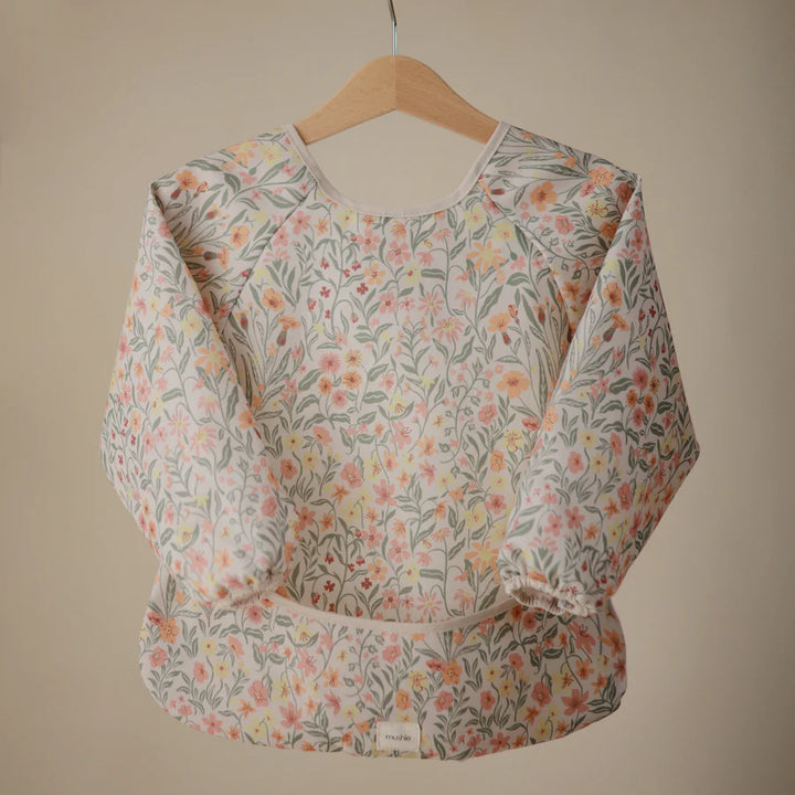 Stylish and functional, these Mushie Long Sleeve Bibs include color options like pastel blooms, ideal bibs for babies.