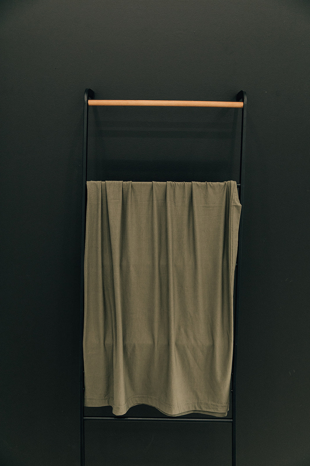 Olive Bamboo Stretch Swaddle draped over a crib rail, a soft stretchy receiving blanket for baby boys and girls.