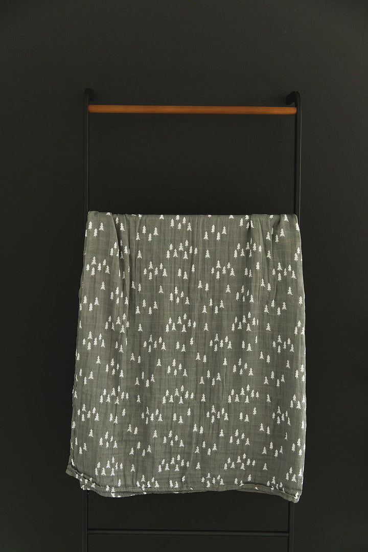 Wrapped around a sleeping newborn, the Pines Muslin Swaddle Blanket from Mebie Baby.