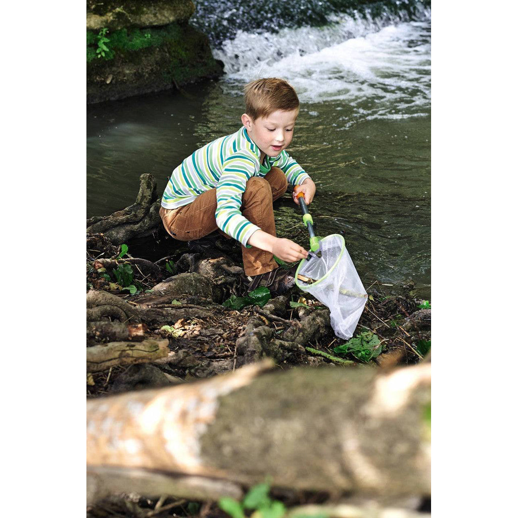 Child playing outdoors with mesh net, collecting sticks.