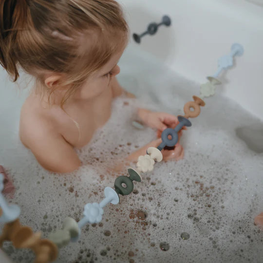 toddler playing with mushie daisy connect suction bath toys in bubble bath 