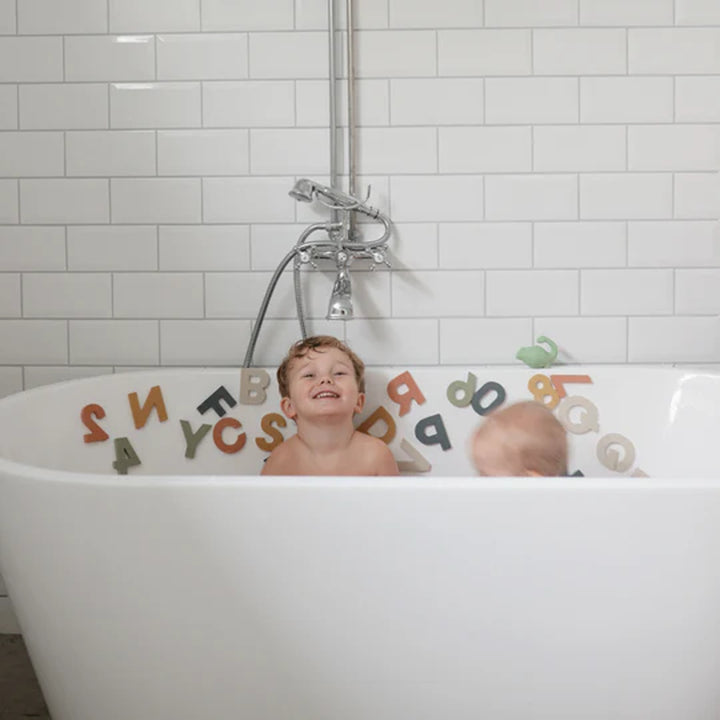 Mushie Letters Numbers Bath Play Set in use - child sticking foam alphabet pieces to tiled bath wall