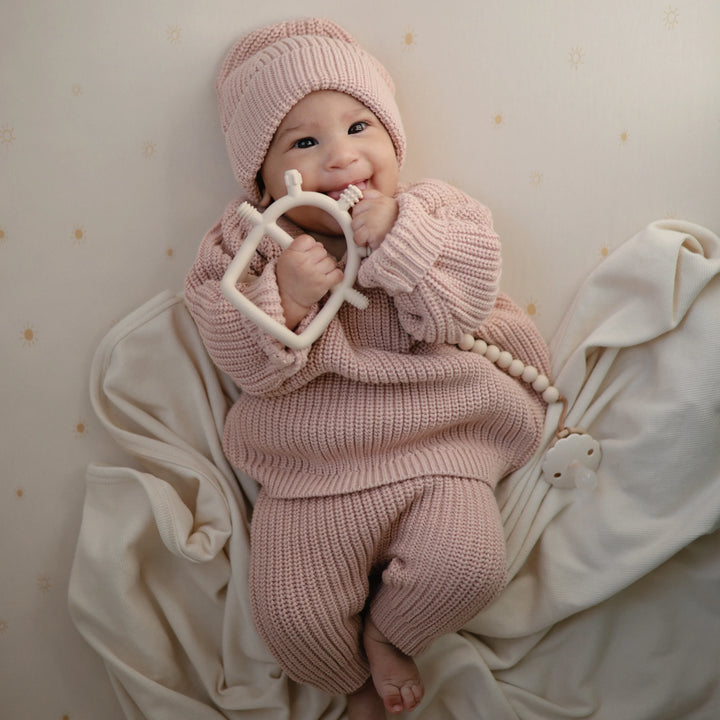 Infant holding easy-grasp Mushie teether toy in pink
