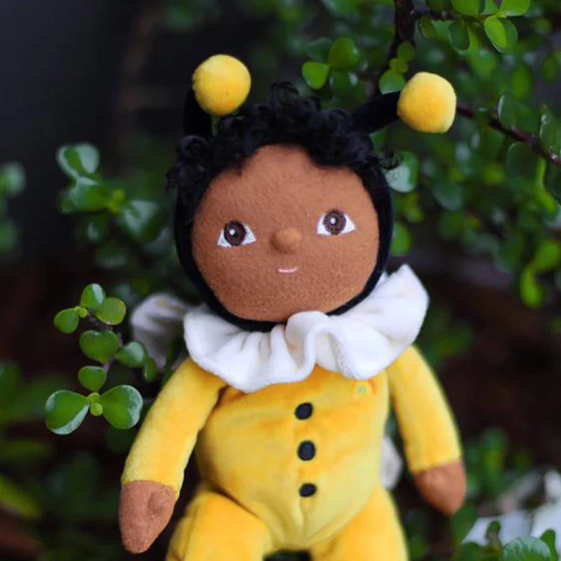 dark-skinned doll for baby in yellow olli ella bumble bee outfit in front of tree 