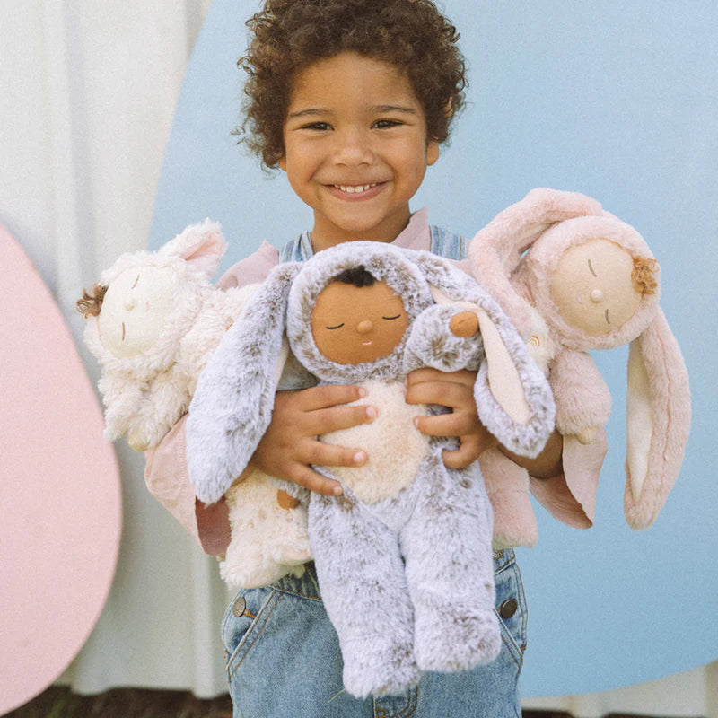 child holding bunny muffin olli ella cozy dinkum to the camera and smiling with her stuffed doll toy 