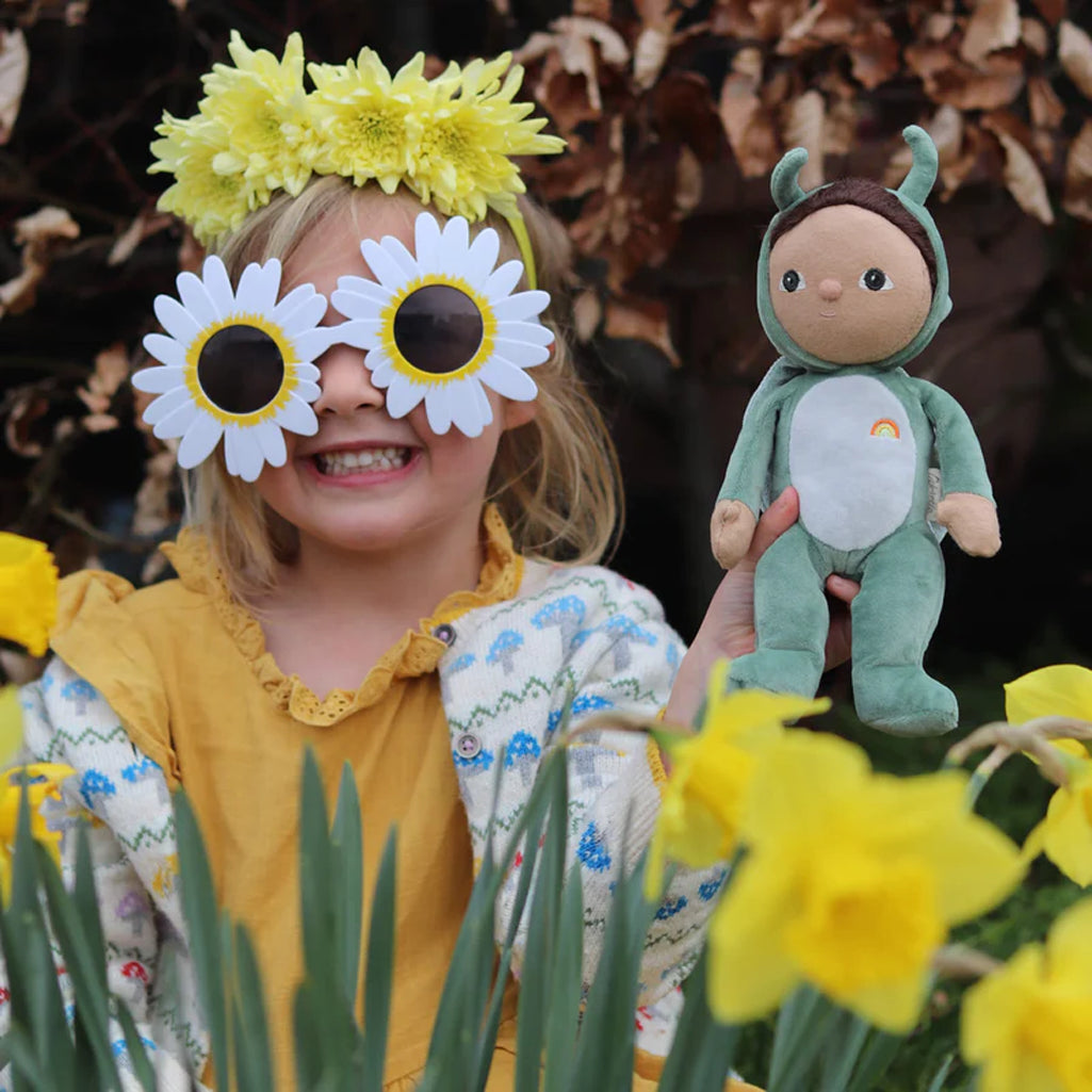 child in sunflower outfit showing off brunette soft baby safe doll in green grasshopper utfot with oli ela logo 