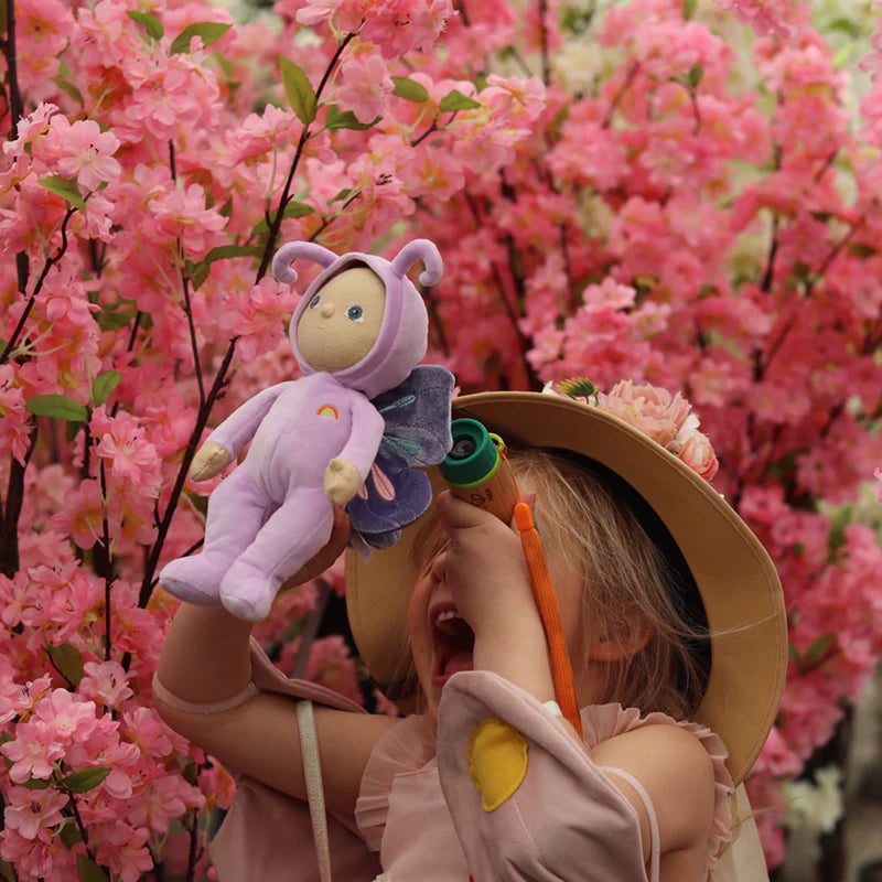 dinky dinkums ollie ella betty butterfly stuffed animal raised up by child in front of pink bush staring with neutral expression upwards 