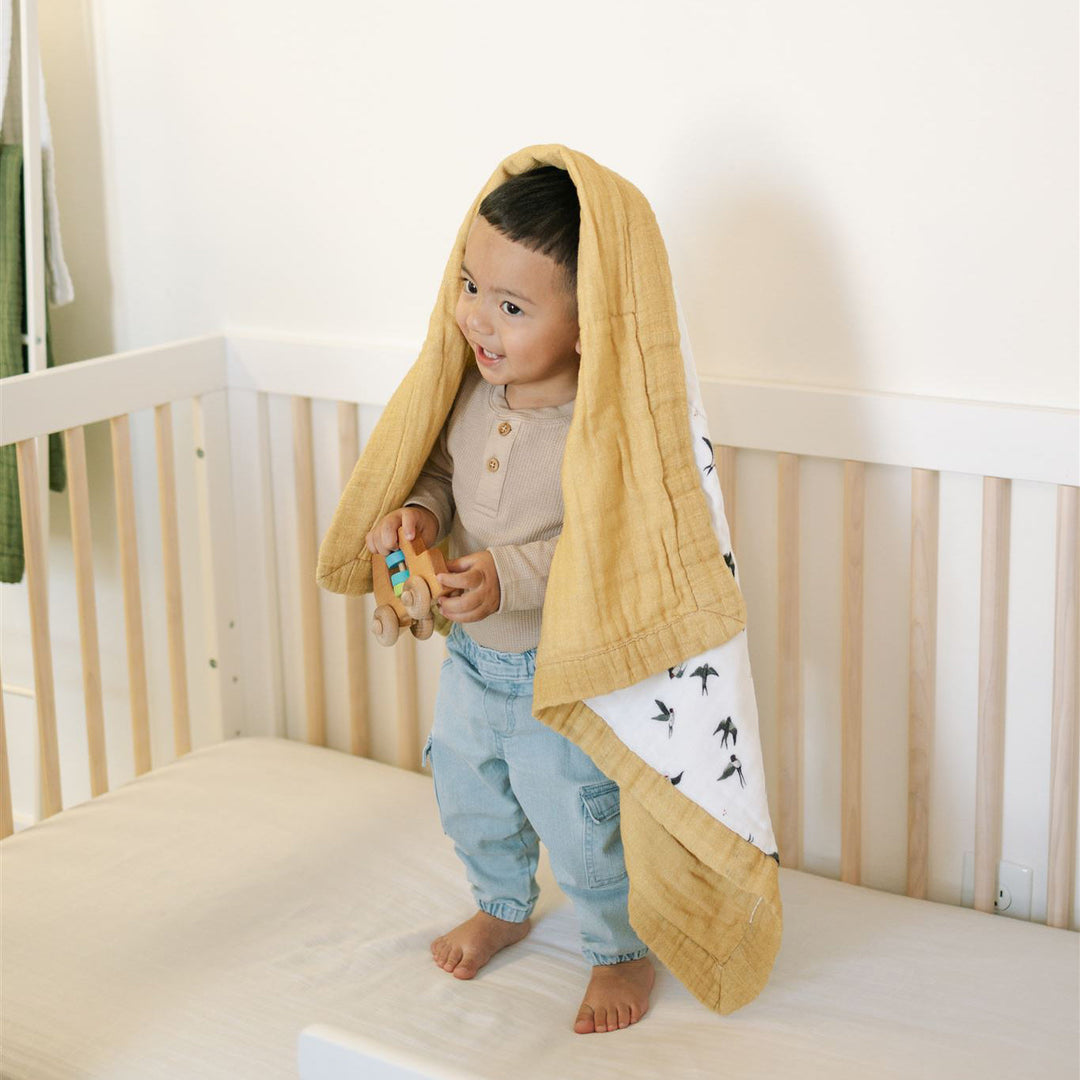 Little Unicorn Organic Cotton Muslin Baby Quilt - Swallows draped on a crib, a charming baby quilt that blends softness with timeless style.