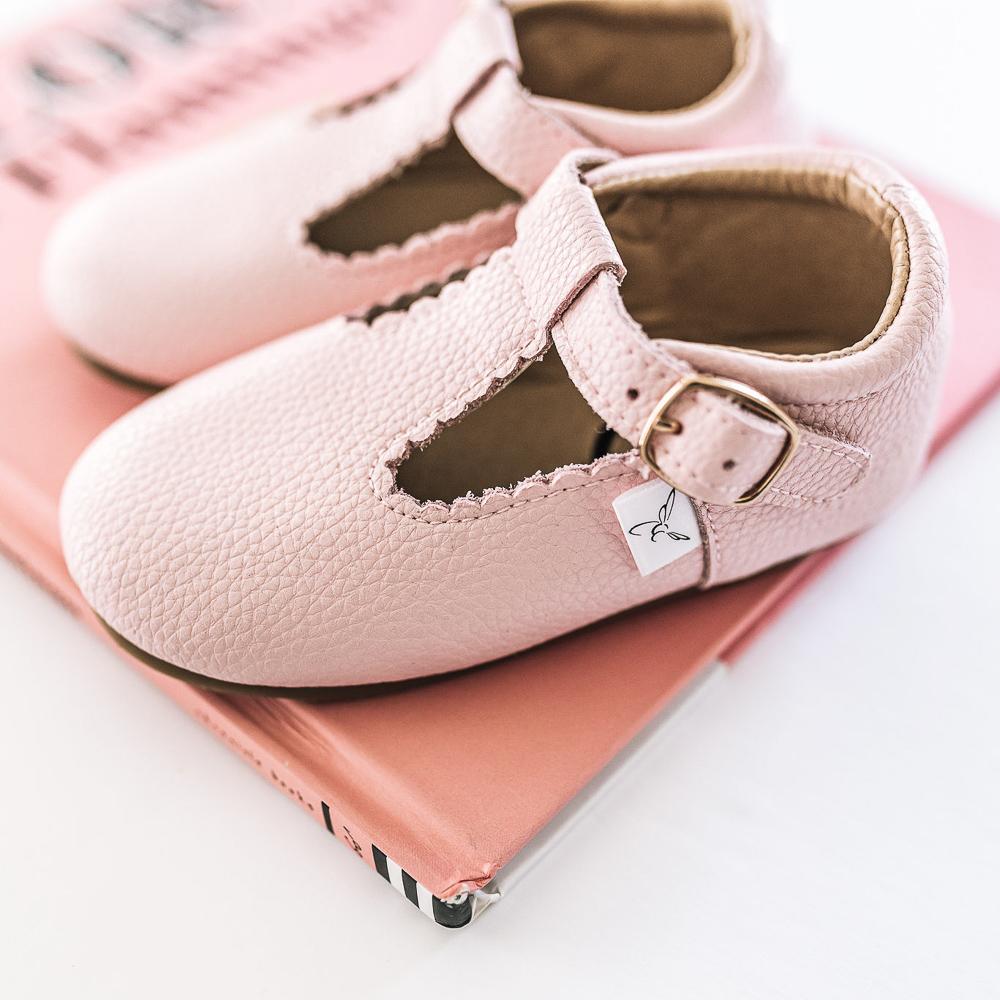  Little Love Bug Company pink leather T-bar shoes sitting on a book.